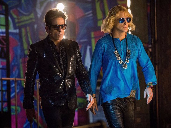 A queer Halloween costume for 2023. The image shows Ben Stiller and Owen Wilson appearing as their characters – Zoolander and Hansel from the film Zoolander. Stiller is wearing shades, a sparkly all black suit and also a black glove on his right hand. Hansel is wearing black leather trousers, a bright blue long sleeved top, sunglasses and a large necklace. Both are walking side-to-side.