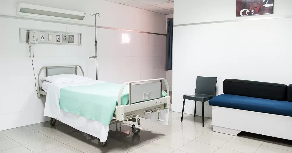 This article is about a ban on trans women from female hospital wards in the UK. In the photo, a hospital room with a bed with a green cover, a chair and a sofa.