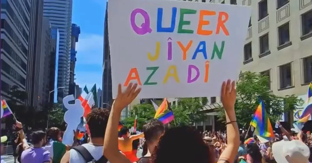 Several people at a protest, one is holding a sign that reads Queer Jivan Azadi'. In this piece, we explore the collective queer that is fighting against censorship in Iran