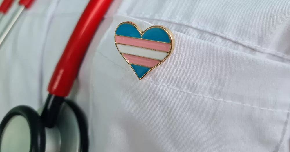 TENI Will be running training sessions aimed at healthcare professional. The image shows a heart shaped badge, pinned to the breast pocket of a white lab coat. In the background, a red stethoscope is visible.
