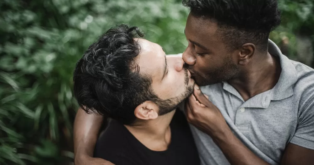 This article is about why people kiss. In the photo, two people kissing with a background of green leaves.