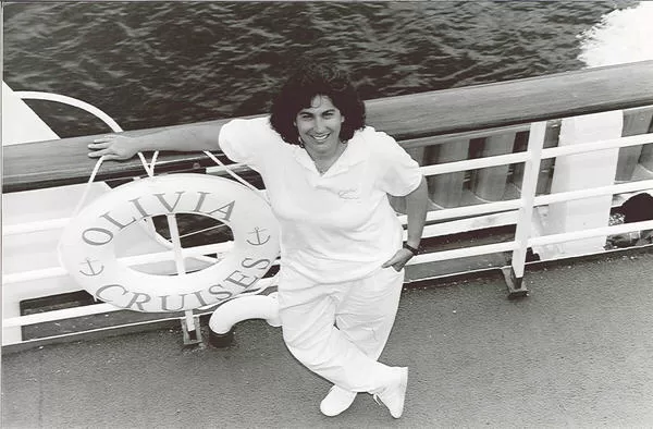 Olivia Lesbian Travel Cruise photo featuring the founder and president, Judy Dlugacz. The image shows Judy standing on the deck of the cruise ship, dressed all in white and the view of the sea behind her.