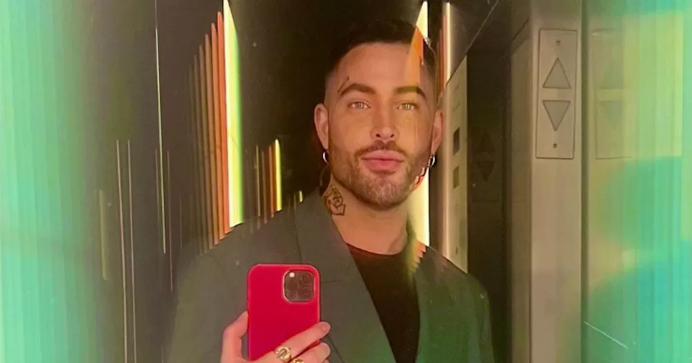 Mirror selfie of hairstylist Andrew Fitzsimons. He is shown from the chest up, pouting slightly and holding a red phone which he is taking the photo with.