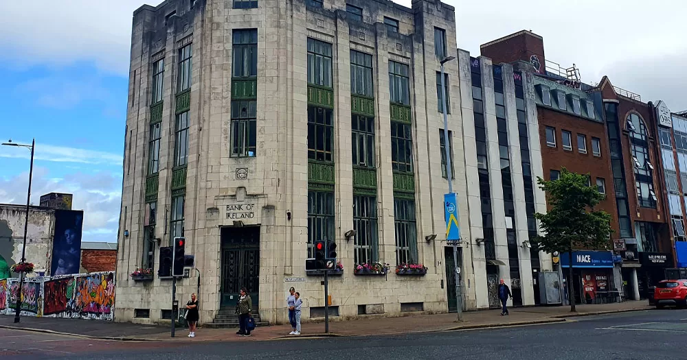 The image shows an art deco building on the corner of North Street in Belfast, near where an alleged homophobic assault occurred. The building's main door is positioned on the corner with the words "Bank of Ireland" above it. The windows stretch the full height of the building in slim columns.