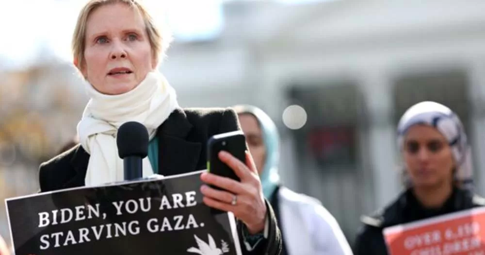 Photo of Cynthia Nixon holding a sign at a hunger strike that says Biden You Are Starving GAZA.
