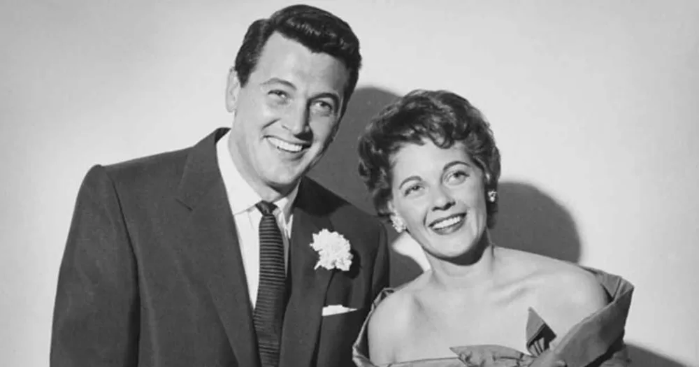 Rock Hudson and Phyllis Gates, in an example of a lavender marriage, smiling for the camera in a black and white photo.