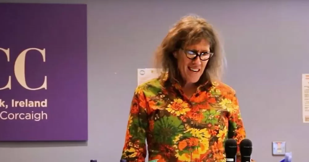 The image shows academic Susan Striker delivering a keynote speech at the Lesbian Lives Conference 2024. She is wearing a flowery shirt in browns, oranges and greens.