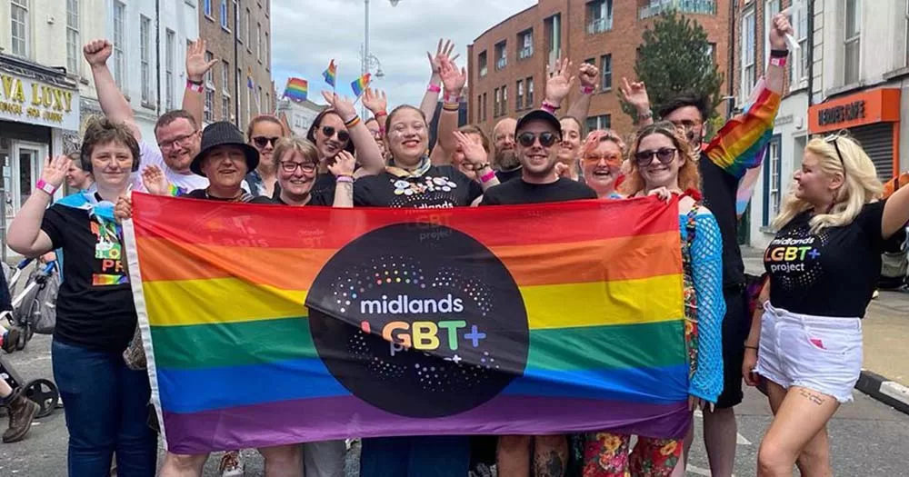 Photograph of people posing with Midlands Pride flag, this week the Midlands LGBT Project lost their 2024 funding.