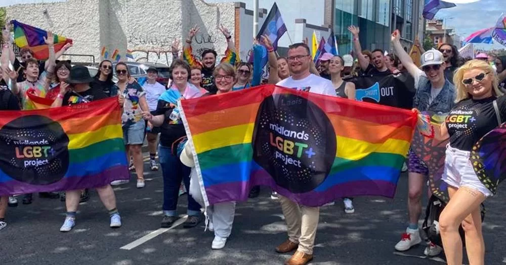 Photograph of a group of people carrying Midlands Pride flag, the article is about the group's funding for 2024.