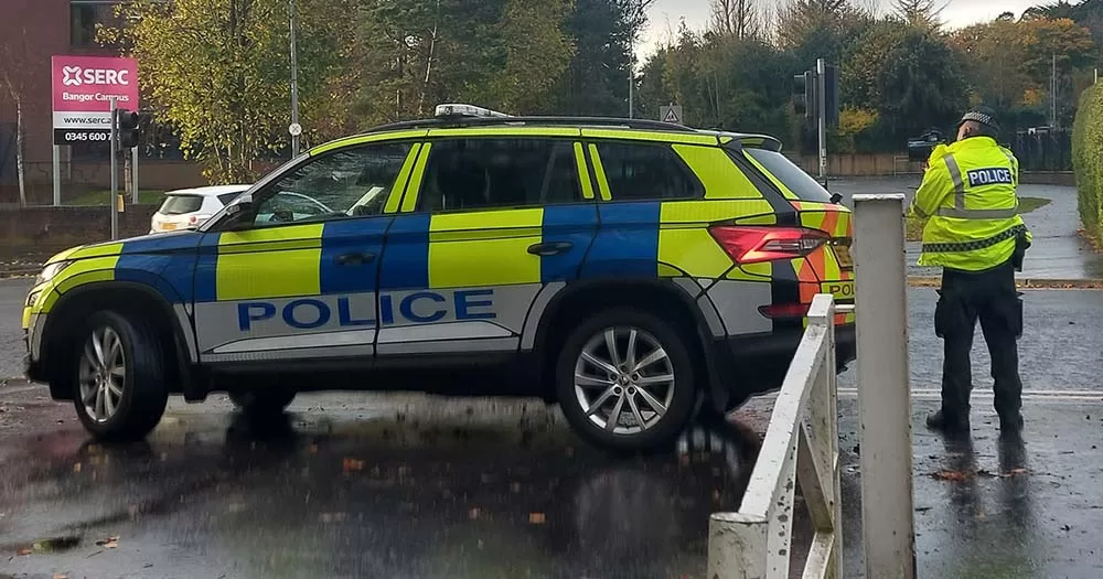 Photo of Northern Ireland police officer standing beside police car.