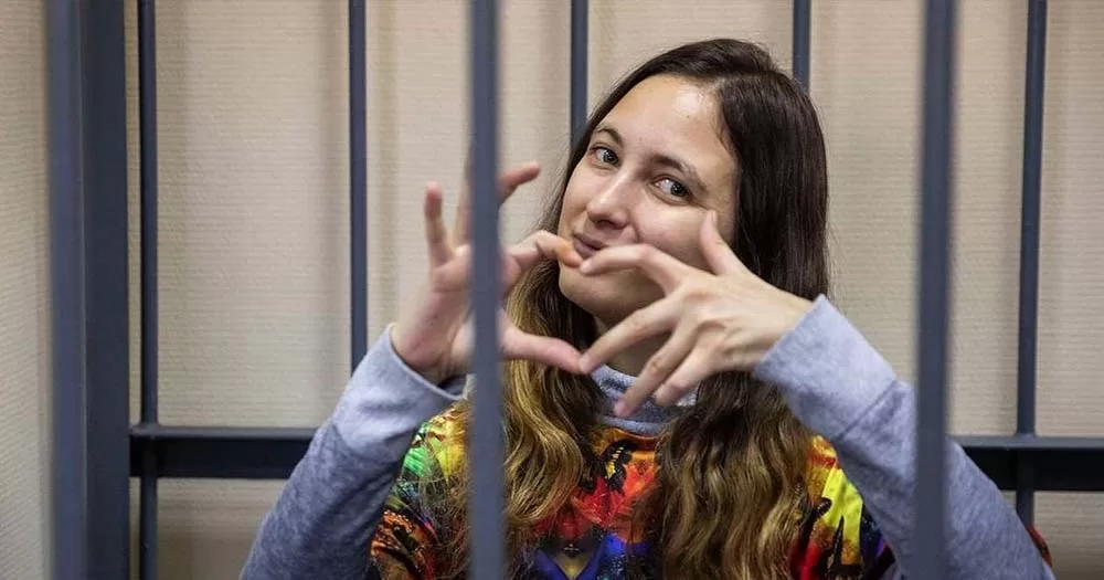 Russian lesbian activist Sasha Skochilenko poses and makes a heart symbol with her hands from behind bars