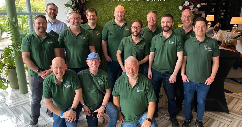 Dublin Gay Men's Chorus poses for a group photo. All members of the group wear green polo t-shirts and smile at the camera.