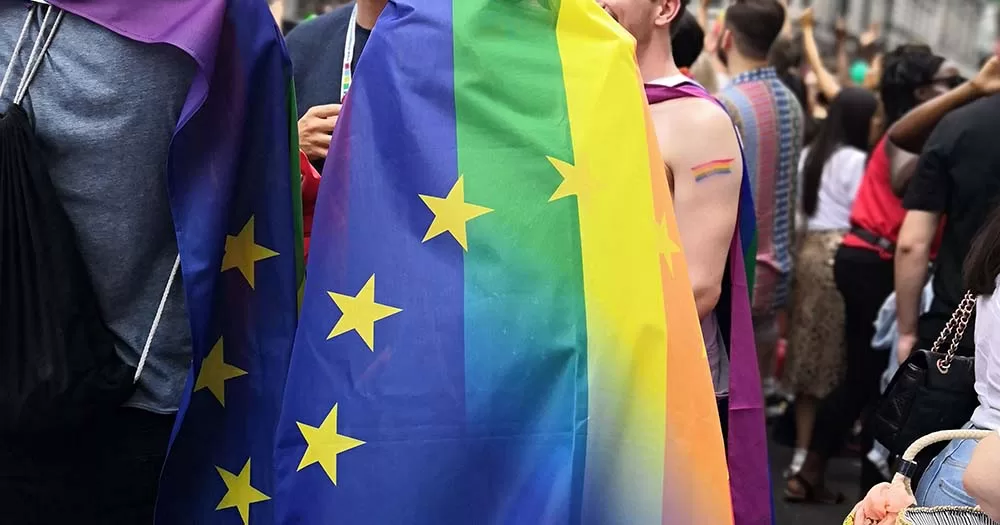 EU and LGBTQ+ blended flag draped around a person's shoulders.