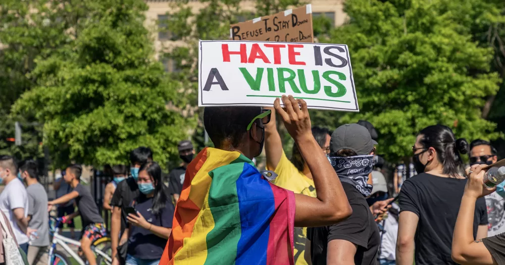 This article is about Irish people's perception of hate crime. In the photo, a person wearing a Pride flag as a cape and holding a sign that reads "Hate is a virus".