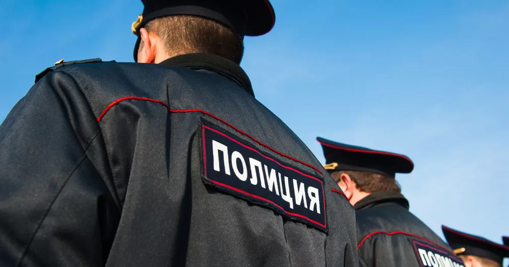 The image shows the back of a Russian policeman following a raid on a gay bar. The photograph is shot from a low angle looking upwards at the back of the uniform into a blue sky.