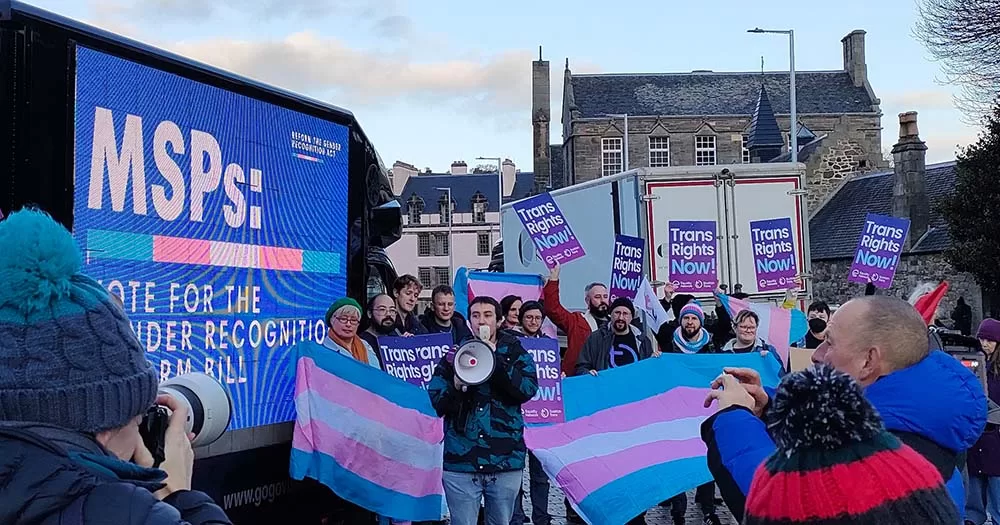 People stand outside Scottish parliament with trans flags and signs advocating for the gender recognition bill