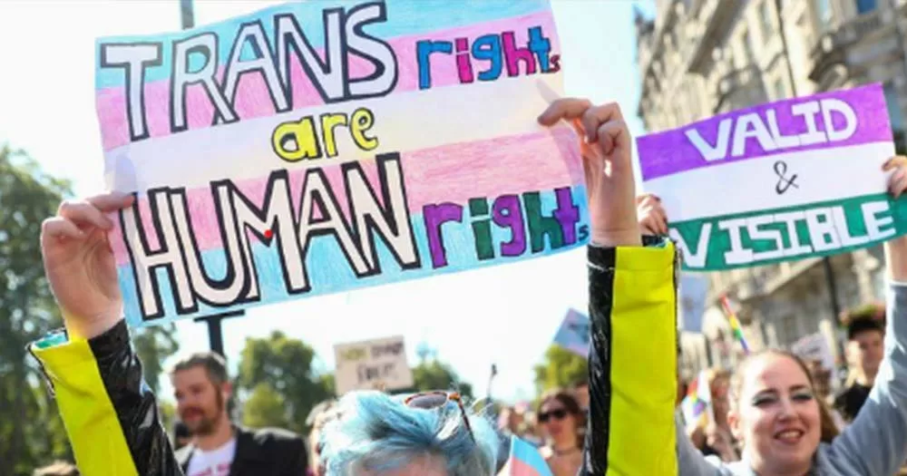 Photo of arms holding Trans rights are human rights sign representing response to new UK trans guidelines for students.