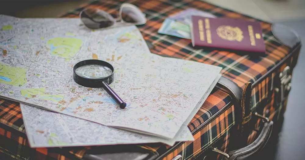 A plaid suitcase with a magnifying glass, map and passport on it.