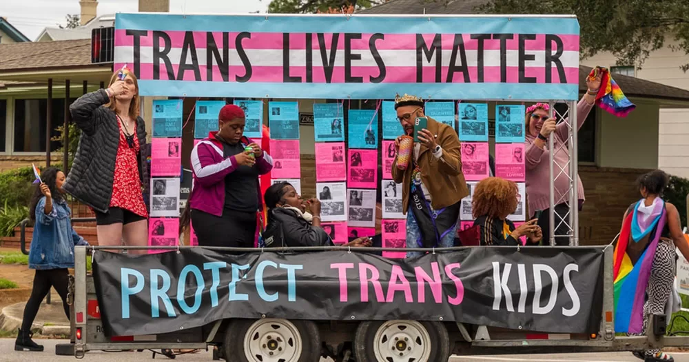 The UK has announced it will no longer accept gender recognition certs from countries that allow self-identification. The image show a group of gender non-conforming people on a float with banners that read "Trans Lives Matter" and "Protect Trans Youth".