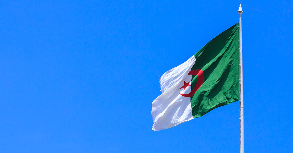 The flag of Algeria, which is now on Ireland's safe countries list. The white and green flag is flying on a pole, with a blue sky in the background.