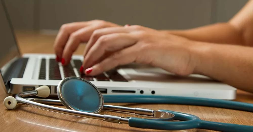 Photograph of a stethoscope resting next to a laptop computer representing LGBTQ+ healthcare