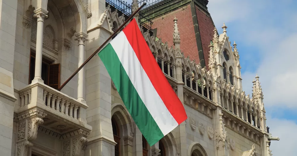 This article is about Hungary refusing to change anti-LGBTQ+ laws condemned by the EU. In the photo, a Hungarian flag flying from a building.