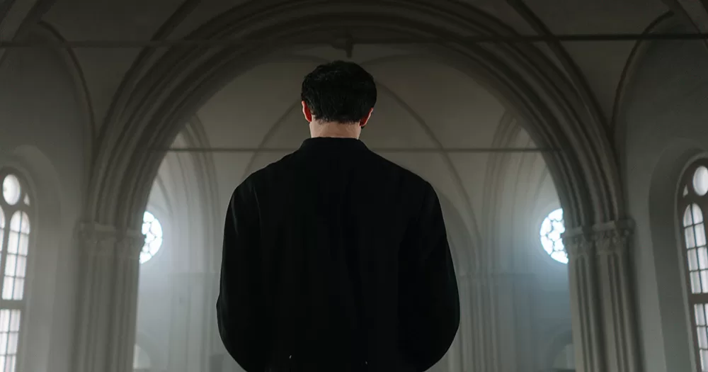 This story is about a priest who has been charged after allegedly organising a gay orgy. The image shows the back of a priest in a black cloak, standing in a church.