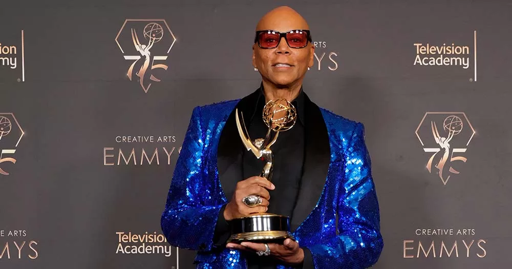 Photograph of RuPaul wearing blue sequin blazer and posing with Emmy award
