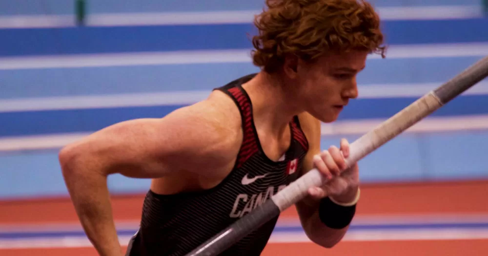 Action shot of Shawn Barber pole vaulting. His side profiled is photographed from the stomach up, as he runs with a pole in his hands.