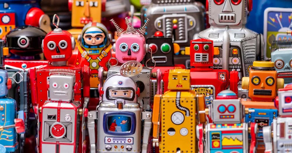 The image shows a collection of toy robots. They are mainly made from coloured tin and are a multicoloured mix of shapes and sizes.