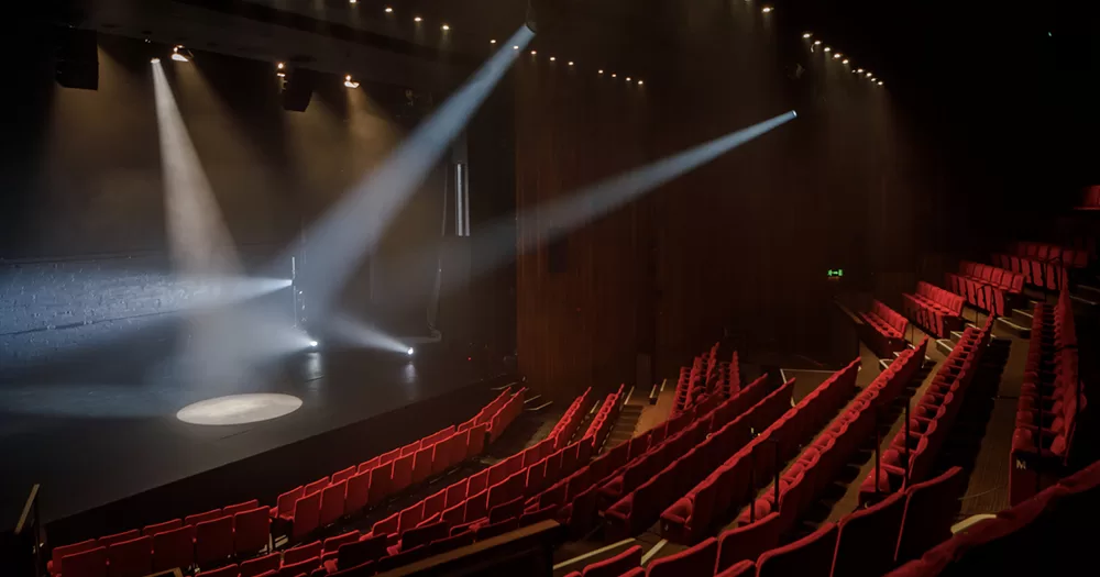 The auditorium of the Abbey Theatre, which is offering Backstage Tours. Lights are on on the stage and red seats face the stage.