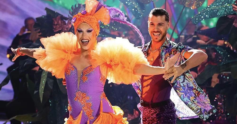 Blu Hydrangea and pro Simon Arena performing a dance that earned them a perfect score on Dancing With The Stars. Both are wearing bright purple and orange costumes.