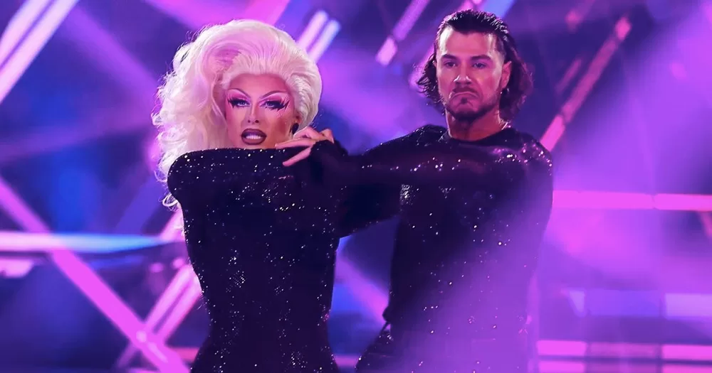 Blu Hydrangea and pro-partner Simone Arena on Dancing with The Stars, performing on RuPaul's song 'Sissy that Walk' wearing matching black and sparkling costumes with blue and purple lights in the background.
