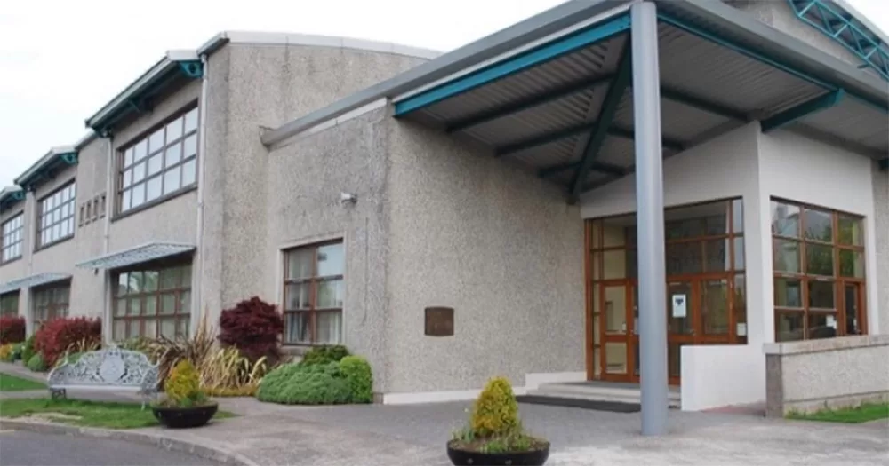 Exterior of Cork school, Gaelscoil Uí Riada, which apologised after a guest speaker went on an anti-LGBTQ+ rant. The image shows the exterior of a grey building with blue accents and some plants on the ground.