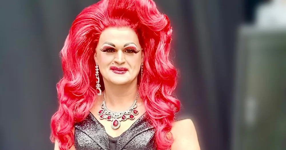 An image of Dame Stuffy who was targeted with homophobic abuse. The drag queen wears a bright red wig, red and silver jewellery and a black sparkly dress.