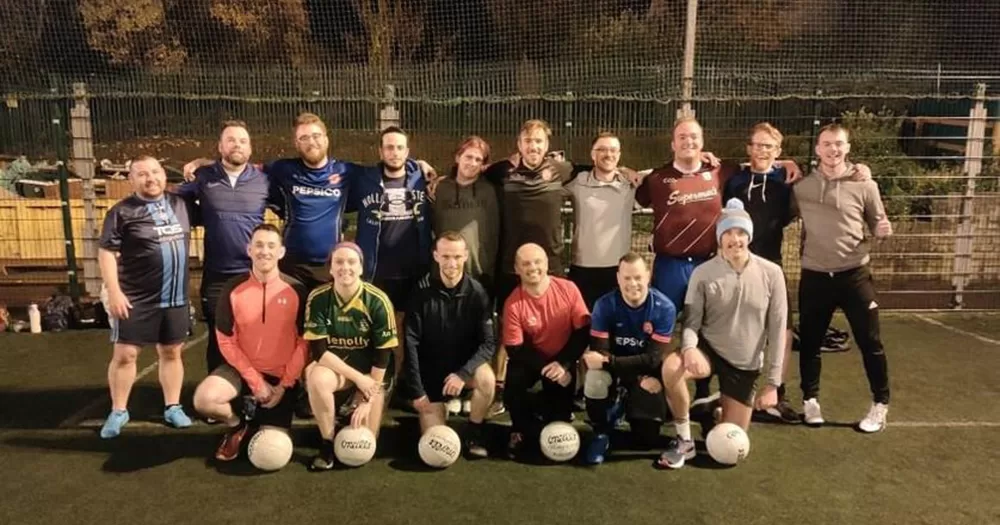 Team photo of Laochra Aeracha, the first LGBTQ+ GAA team in Cork. The GAA players pose after a training session, with one row of people crouched at the front, and a row of people standing behind them.