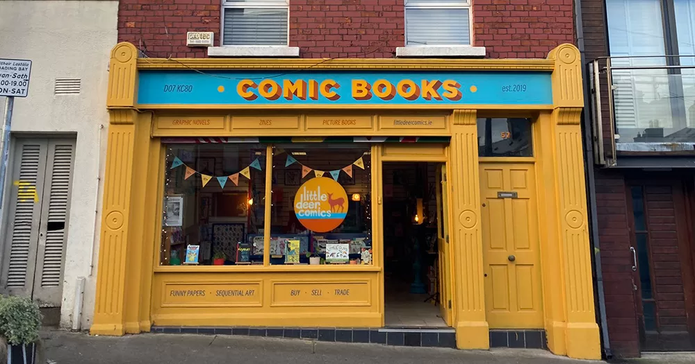The exterior of Little Deer Comics. It is a yellow store front with blue and yellow signage.