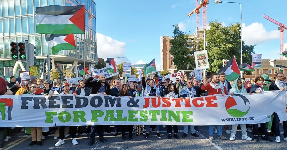 A demostration for palestine held in Dublin, with people carrying Palestinian flags and a banner that reads 'Freedom and justice for Palestine'.