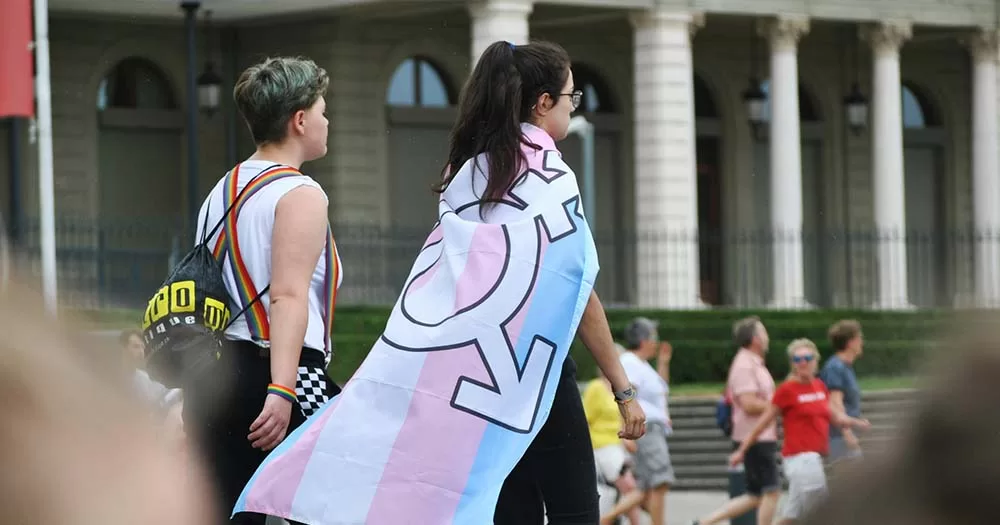 Photo of person walking with transgender flag on their back, representing largest ever transgender survey.
