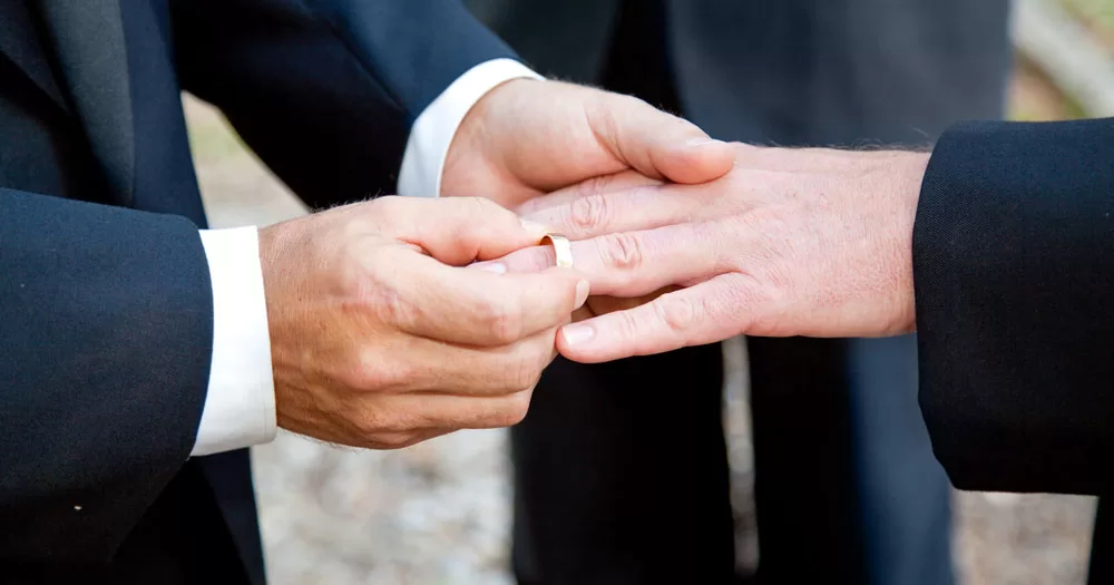 Greece has held its first same-sex wedding. The image shows two men's hands. The person on the left is putting a plain gold wedding ring on the finger of the person on the right.