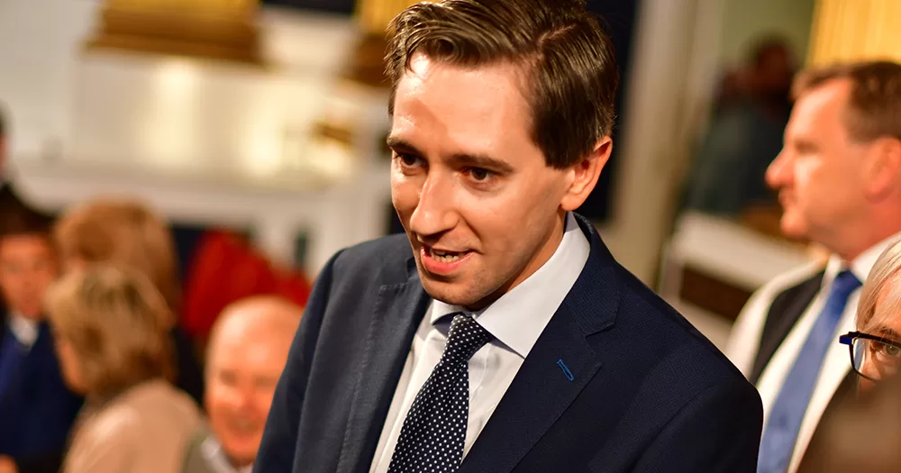 Simon Harris, who is set to become Taoiseach in April, in a room with other people speaking to someone off camera.