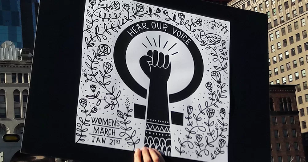 A sign from an International Women's Day march. It shows a women's protest symbol, with the words "Hear our voice".
