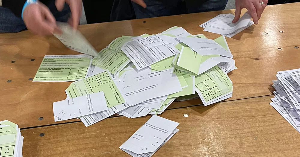 Ballot papers from the referendums in Ireland on Family and Care. The green and white slips are being counted in a pile on a wooden table.