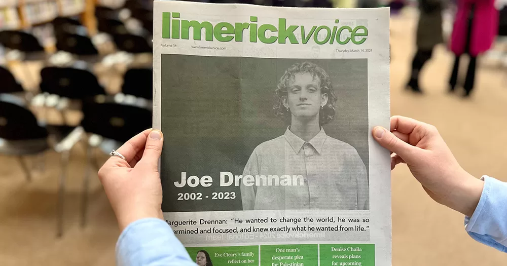 Photo taken at the launch of the Joe Drennan Memorial Competition for Inclusive Journalism. It shows the cover of the Limerick Voice newspaper, featuring a black and white image of Joe. Two hands hold the newspaper up close to the camera.