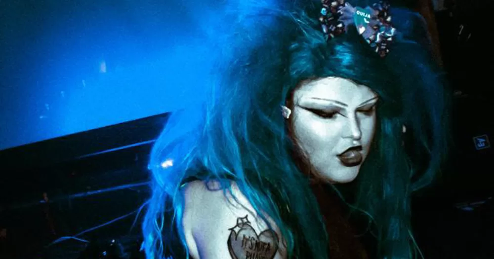 An image of Boo Boo Oopsie, organiser of Making a Scene. The drag queen is photographed in blue light, wearing a blue wig and black eyeliner and lipstick.