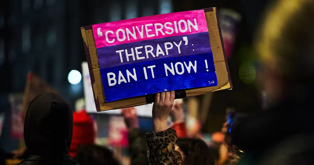 This article is about a conversion therapy ban in New South Wales, Australia. In the photo, a hand holding up a sign that reads "conversion therapy, ban it now".