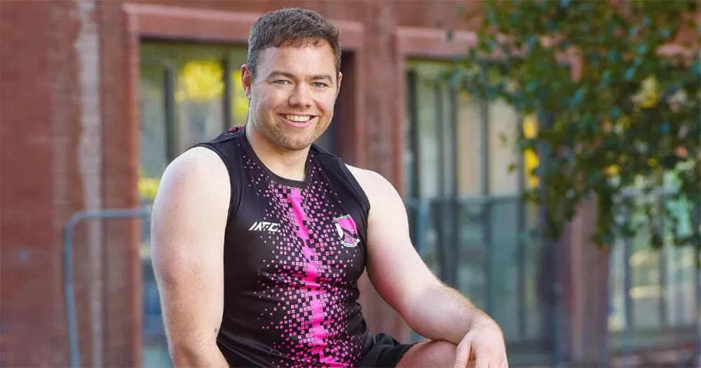 Queer Irish influencer Cian Ó Gríofa photographed from the waist up in a sleeveless GAA jersey. He smiles and looks at the camera.