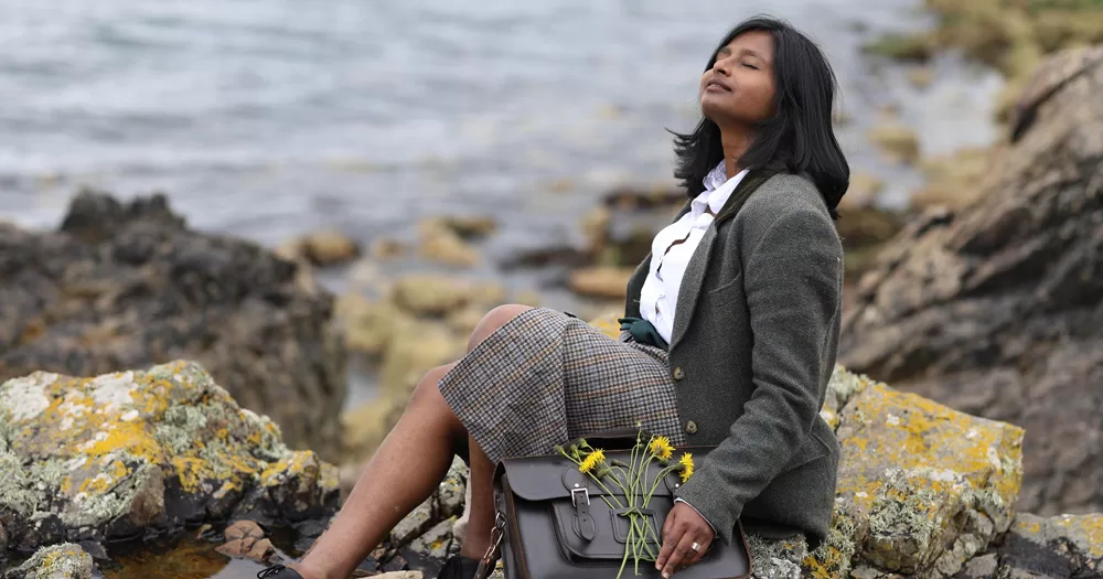 Activist Dr Shubhangi Karmakar, who advocated for yes no vote in the family and care referendums, sitting on a rock with the sea in the background.