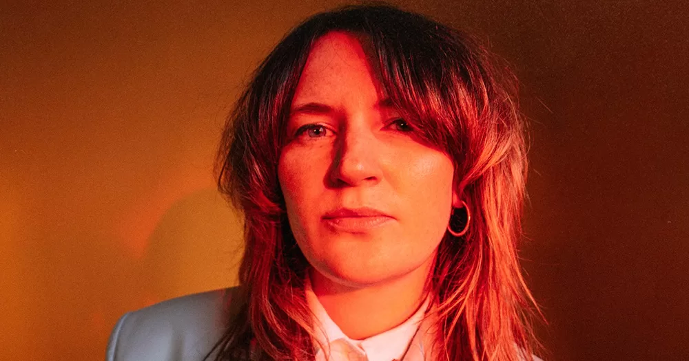 A press image of SAOIRSE, the DJ headlining Mother's Cultúr Club. SAOIRSE is shown from the shoulders up, photographed in red/orange light with her hair down.