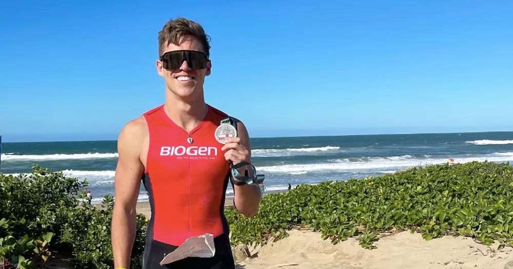 Zimbabwean Olympic swimmer Sean Gunn posing with a medal in front of a beach.